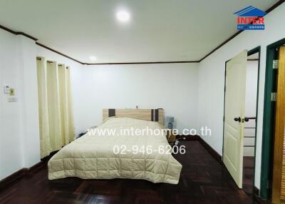 Bedroom with a bed, light colored bedspread, white walls, and wooden floor