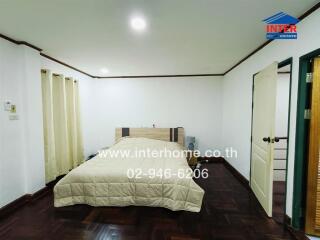 Bedroom with a bed, light colored bedspread, white walls, and wooden floor