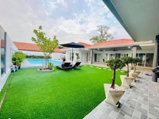 Spacious outdoor area with artificial grass, potted plants, and a swimming pool.
