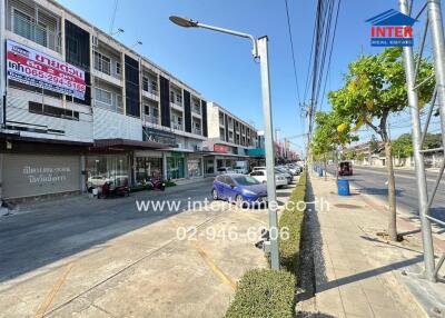 Street view of buildings including shops, cars parked, and street lamps