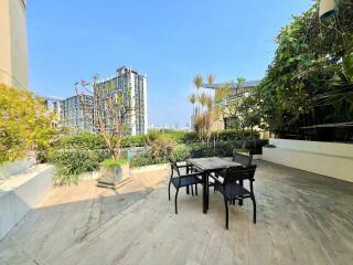 Outdoor patio with table and chairs, surrounded by greenery and city view