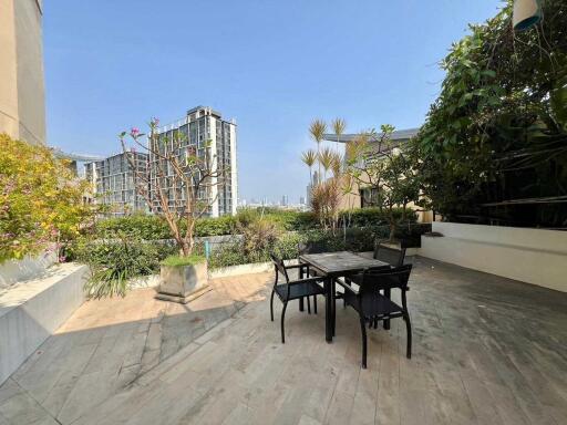 Outdoor patio area with table and chairs, greenery, and a city view