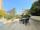 Spacious outdoor patio with table and chairs, lush greenery, and city view