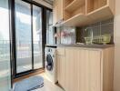 Modern kitchen area with light wood cabinets, a washing machine, and a small balcony.