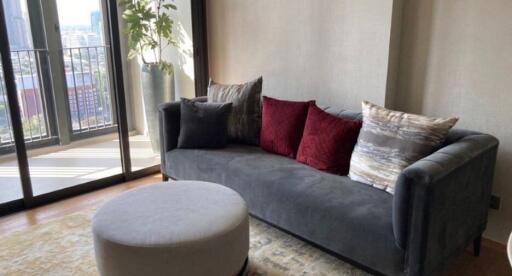 Modern living room with a large window, gray sofa, round ottoman, and decorative cushions