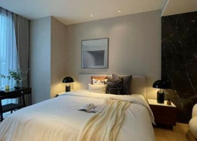 Modern bedroom with large bed, bedside tables with lamps, desk by the window, and comfortable chair