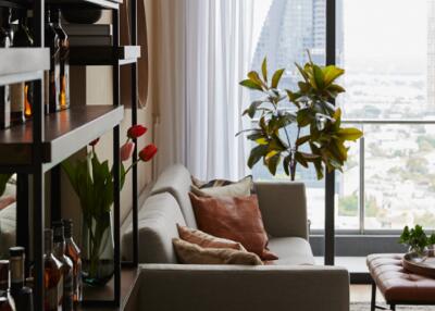 Cozy living room with a sofa, shelves, indoor plants, and a large window with a view of the city
