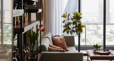 Cozy living room with a sofa, shelves, indoor plants, and a large window with a view of the city