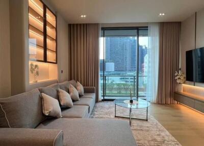 Modern living room with a large grey sofa, glass coffee table, wall-mounted TV, and a view of the city through a large window