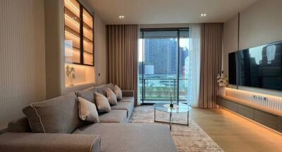 Modern living room with a large grey sofa, glass coffee table, wall-mounted TV, and a view of the city through a large window