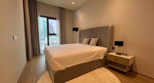 Spacious bedroom with a large bed, modern furnishings, and a window with city view