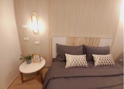 Modern bedroom with a neatly made bed, two decorative pillows and a bedside table with a lamp, plant and photo frame.