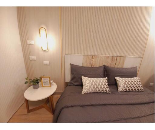 Modern bedroom with a neatly made bed, two decorative pillows and a bedside table with a lamp, plant and photo frame.