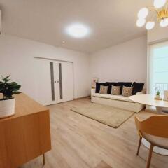 Spacious and modern living room with wooden flooring, a comfortable sofa, a dining table, and contemporary lighting.