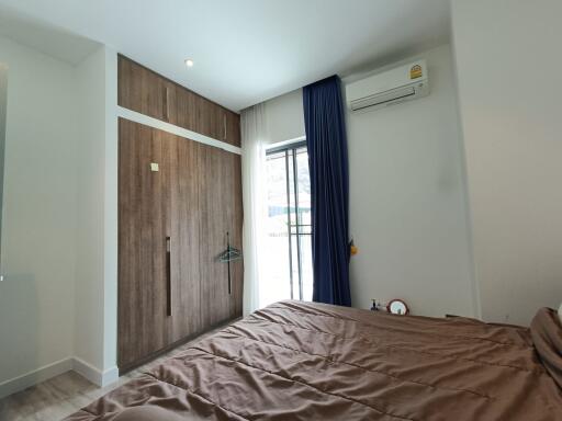 Modern bedroom with a large window, wooden wardrobe, and air conditioning unit