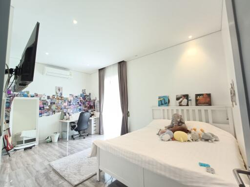 Spacious bedroom with a large bed, wall-mounted TV, desk area, and natural light