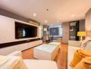 Modern living room with wooden flooring, white furniture, and a large TV