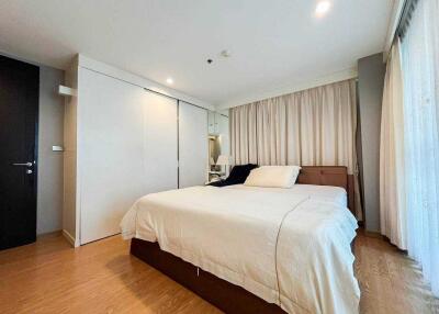 A well-lit bedroom with a large bed, wooden floor, and sliding closet doors