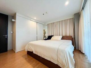 A well-lit bedroom with a large bed, wooden floor, and sliding closet doors