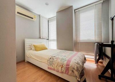 A well-lit bedroom with a single bed, wooden flooring, and window blinds