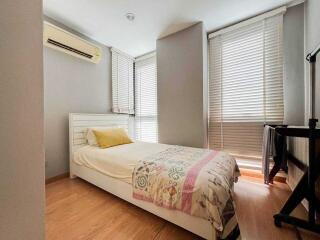 A well-lit bedroom with a single bed, wooden flooring, and window blinds