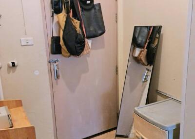 Photo of an entrance area with a door, hanging bags, a freestanding mirror, and a small storage unit.