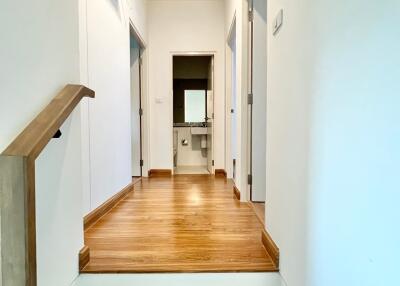 A photo of a hallway with wooden flooring and white walls, leading to rooms.