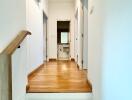 A photo of a hallway with wooden flooring and white walls, leading to rooms.