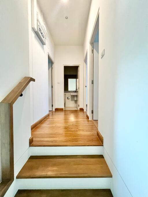 A photo of a hallway with wooden flooring and white walls, leading to rooms.