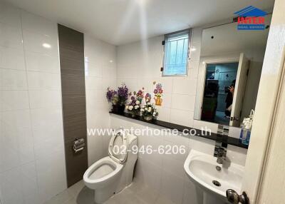 Modern bathroom with white tiles, toilet, sink, and decorative flowers