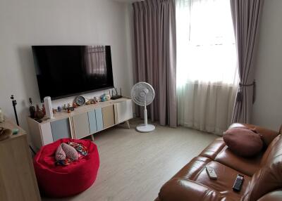 Modern living room with brown leather sofa, flat screen TV, and floor fan