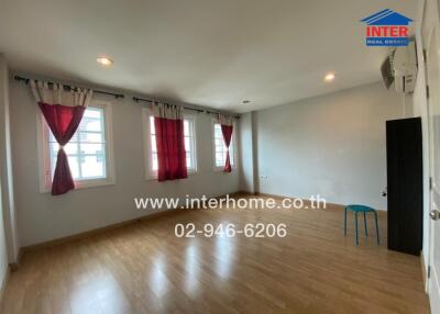 A spacious and unfurnished bedroom with wooden flooring, three large windows with curtains, and overhead lighting.