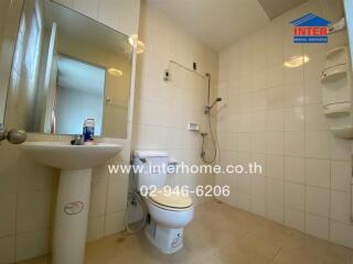 Bathroom with white tiles, a toilet, a sink, a shower, and built-in shelves