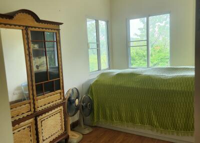 A cozy bedroom with a bed, cabinet, two fans, and large windows