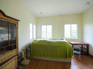 A bedroom with green bedding, wooden furniture, and natural light from multiple windows