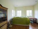 A bedroom with green bedding, wooden furniture, and natural light from multiple windows