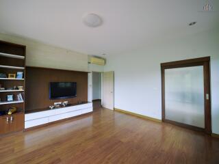 Spacious living room with wooden flooring, built-in shelves, and a wall-mounted TV.