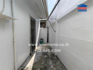 Narrow outdoor passageway with white walls and a utility area
