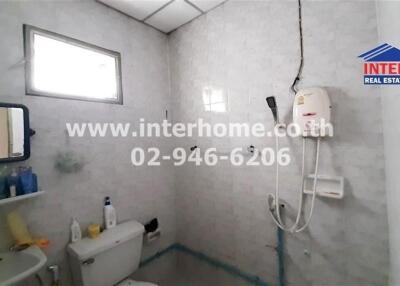 Bathroom with gray tiles, shower system, toilet, small window, and sink with toiletries
