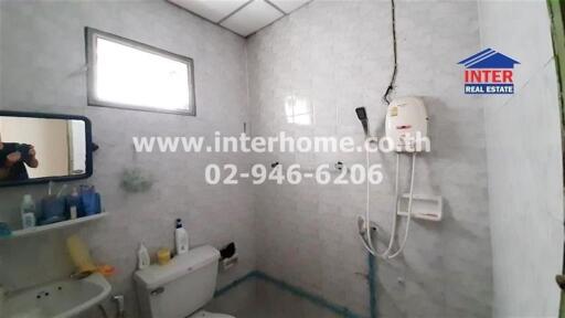 Bathroom with gray tiles, shower system, toilet, small window, and sink with toiletries