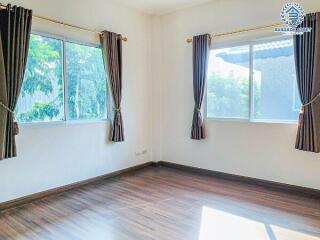 Bright bedroom with wooden flooring and two large windows with curtains