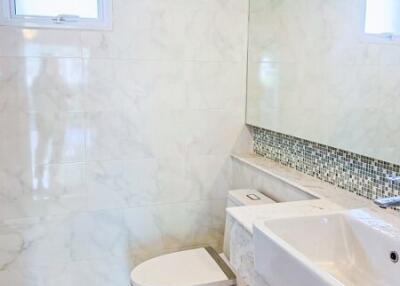 Modern white-tiled bathroom with enclosed toilet, sink, large mirror and window