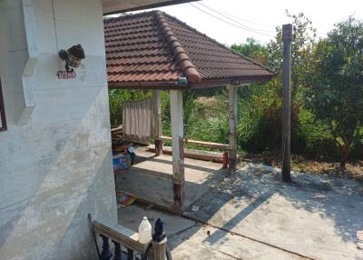 Outdoor area with a cover, house structure visible on the left, trees and greenery around