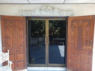 Double wooden doors with intricate carvings opening to a balcony with glass doors