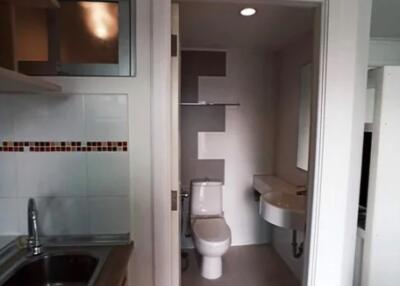 Small bathroom next to kitchen with sink, toilet, and wall-mounted mirror