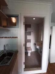 Small bathroom next to kitchen with sink, toilet, and wall-mounted mirror