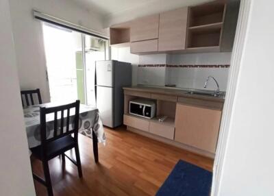 A small kitchen with light wood cabinetry, refrigerator, microwave, and dining table