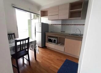 A small kitchen with light wood cabinetry, refrigerator, microwave, and dining table