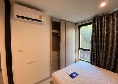 A well-lit bedroom with a large window, air conditioner, and a wardrobe.