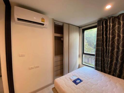 A well-lit bedroom with a large window, air conditioner, and a wardrobe.